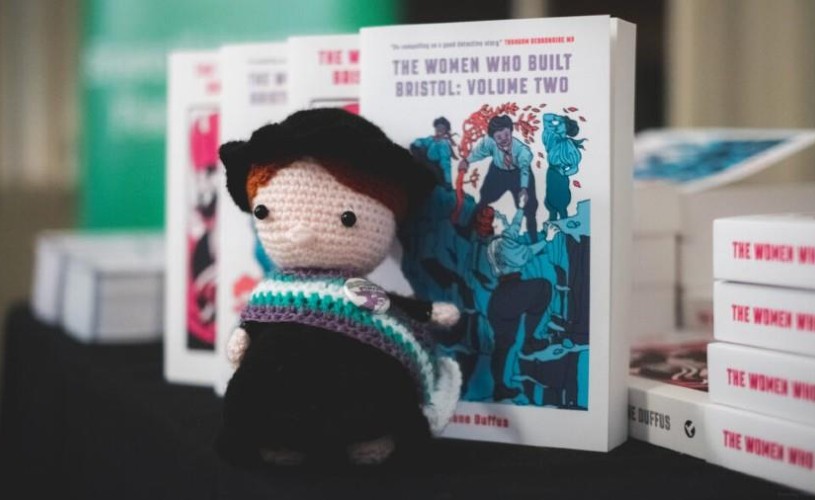 Suffragette style toy in front of copies of 'The Women Who Built Bristol' books